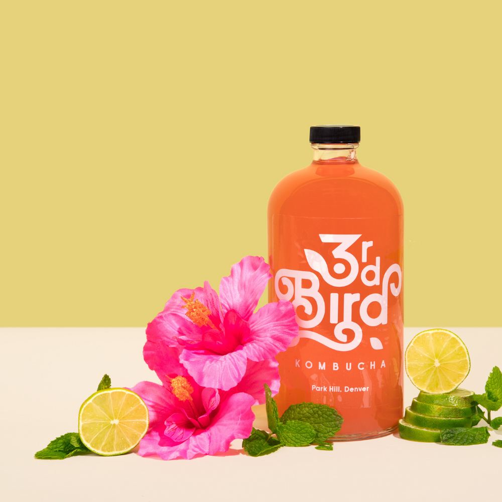 Kombucha bottle next to limes and hibiscus flowers