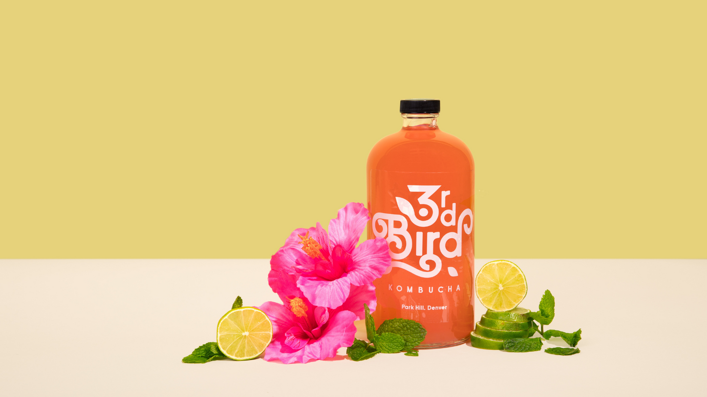 Kombucha bottle next to limes and hibiscus flowers