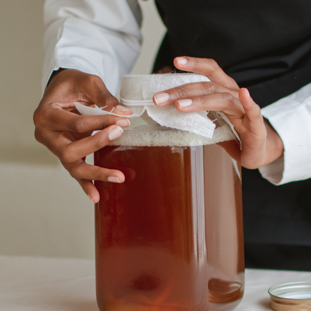 PERSON PUTTING COVER ON HOMEBREWED KOMBUCHA