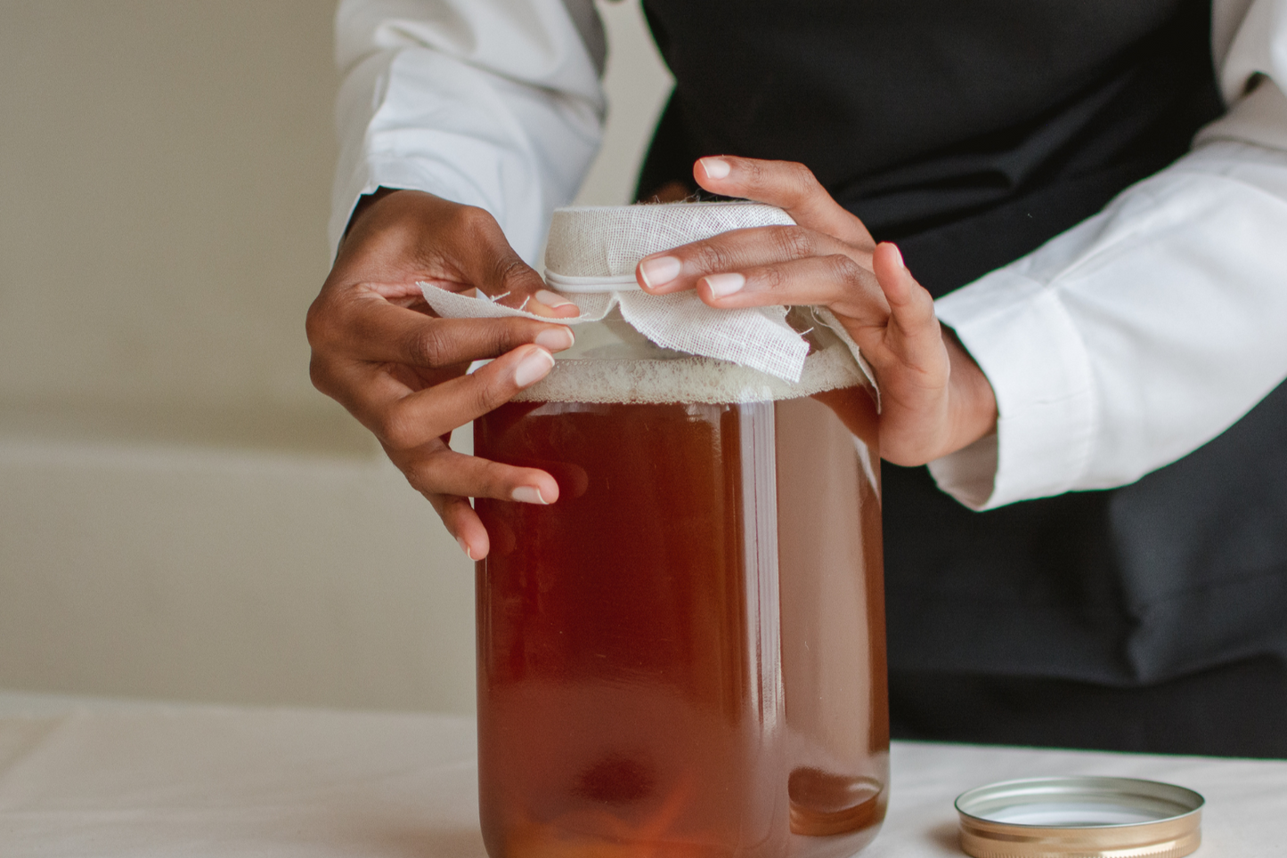 PERSON PUTTING COVER ON HOMEBREWED KOMBUCHA